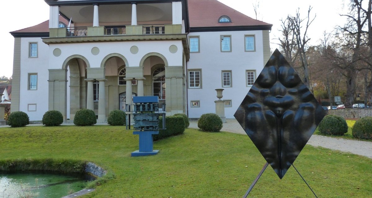 Schloss Dätzingen mit modernen Skulpturen im Vordergrund, umgeben von gepflegtem Rasen und einem kleinen Teich., © Natur.Nah. Schönbuch & Heckengäu Schloss Dätzingen mit modernen Skulpturen im Vordergrund, umgeben von gepflegtem Rasen und einem kleinen Teich., © Natur.Nah. Schönbuch & Heckengäu