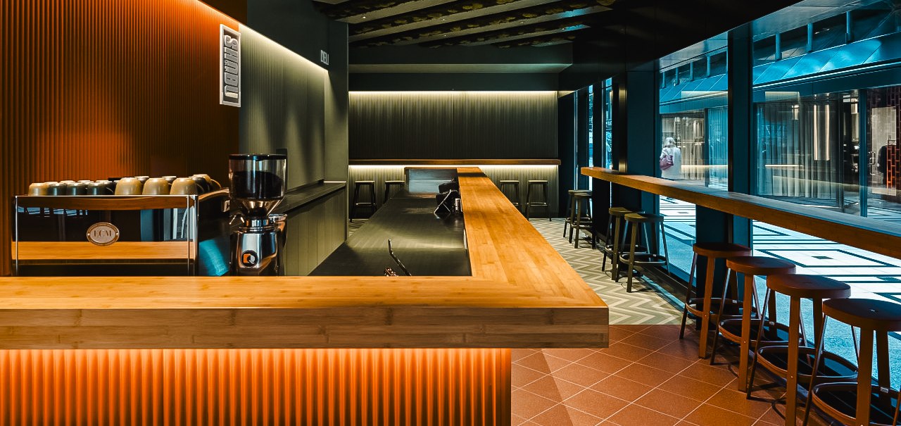 Moderne Bar mit Holztresen, Hockern und stilvoller Beleuchtung in der Shobu Calwer Passage. Dunkle Wände und geometrische Deckenmuster., © Blackbook Studios Moderne Bar mit Holztresen, Hockern und stilvoller Beleuchtung in der Shobu Calwer Passage. Dunkle Wände und geometrische Deckenmuster., © Blackbook Studios