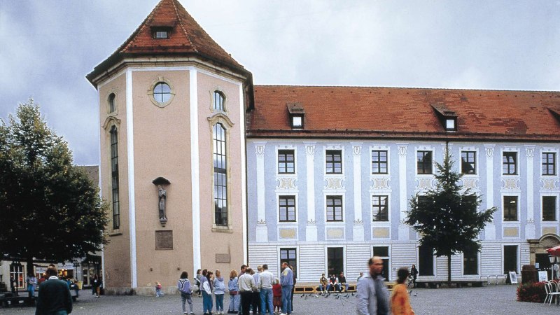 Historisches Geb&auml;ude mit Turm und roten Ziegeldach. Menschen stehen auf einem Platz davor. Der Himmel ist bew&ouml;lkt., &copy; Stuttgart-Marketing GmbH