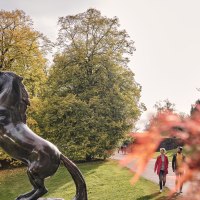 Bronzestatue eines aufsteigenden Pferdes im Höhenpark Killesberg, umgeben von herbstlichen Bäumen und einem spiralförmigen Aussichtsturm im Hintergrund., © SMG, Christoph Düpper