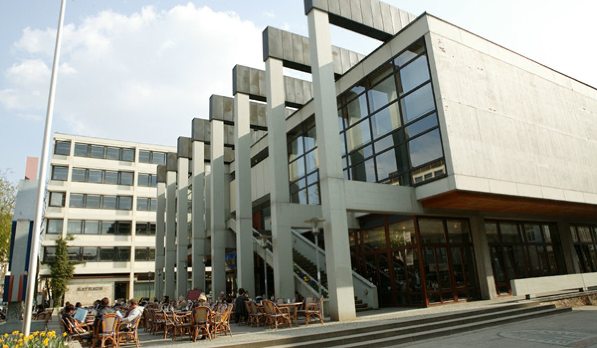 Das Reutlinger Rathaus mit moderner Architektur, Glasfassade und Außenterrasse. Menschen sitzen an Tischen im Freien. Himmel ist leicht bewölkt., © Sphäre Verlag