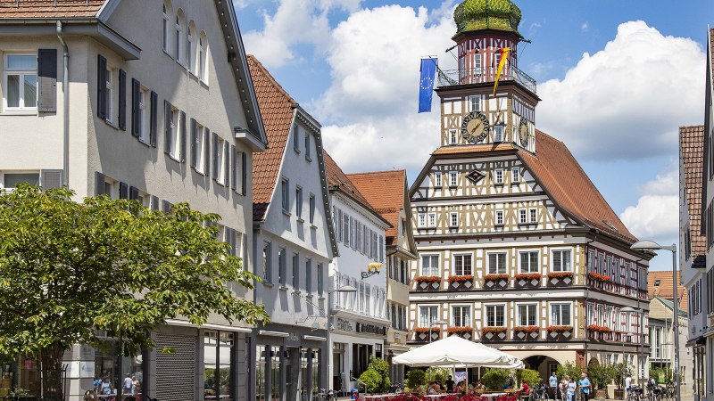 Das Fachwerk-Rathaus von Kirchheim unter Teck mit Uhrturm, umgeben von historischen Gebäuden und einem belebten Platz mit Cafés., © Torsten Wenzler
