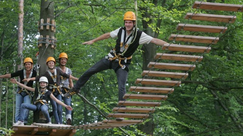 Menschen mit Helmen und Sicherheitsgurten auf einer Hängebrücke im Waldseilgarten Herrenberg, umgeben von grünen Bäumen., © Waldseilgarten Herrenberg Menschen mit Helmen und Sicherheitsgurten auf einer Hängebrücke im Waldseilgarten Herrenberg, umgeben von grünen Bäumen., © Waldseilgarten Herrenberg