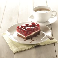 Himbeerschnitte auf einem Teller mit Löffel, daneben eine Tasse Kaffee auf einem Holztisch., © Bäckerei Veit, Victoria Huber