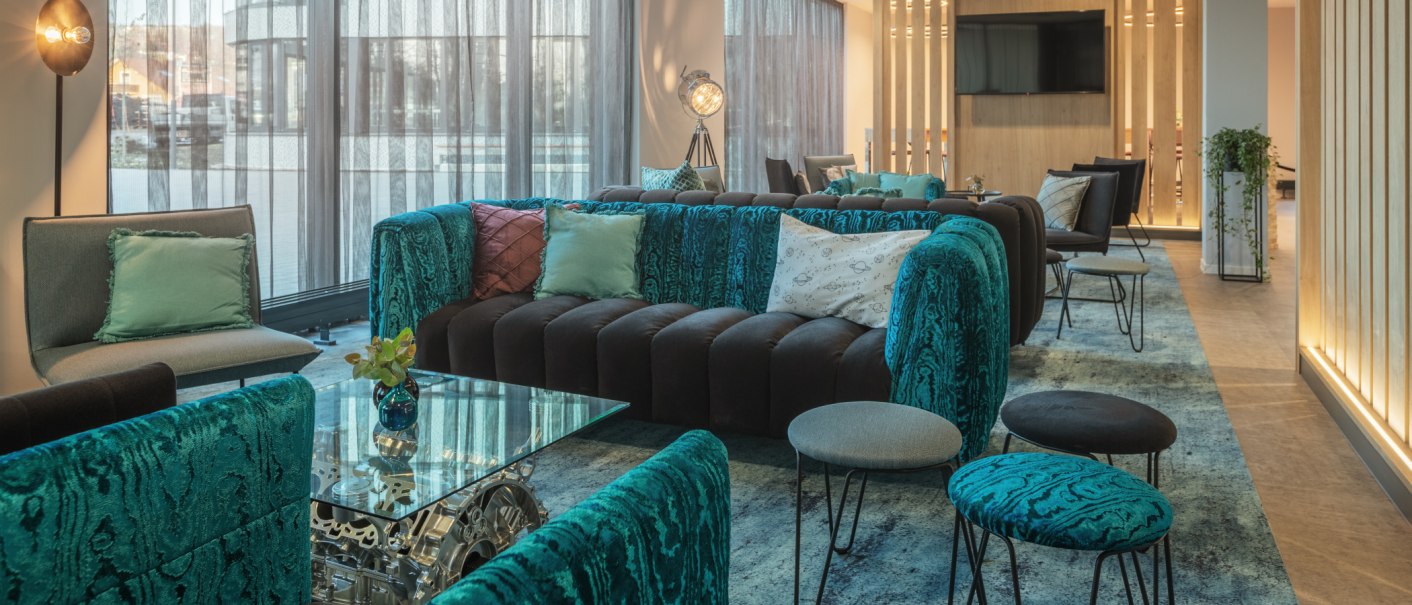 Moderne Lobby mit blauen Sofas, Glastisch, dekorativen Kissen und stilvoller Beleuchtung. Große Fenster lassen viel Licht herein., © Novum Management GmbH Moderne Lobby mit blauen Sofas, Glastisch, dekorativen Kissen und stilvoller Beleuchtung. Große Fenster lassen viel Licht herein., © Novum Management GmbH