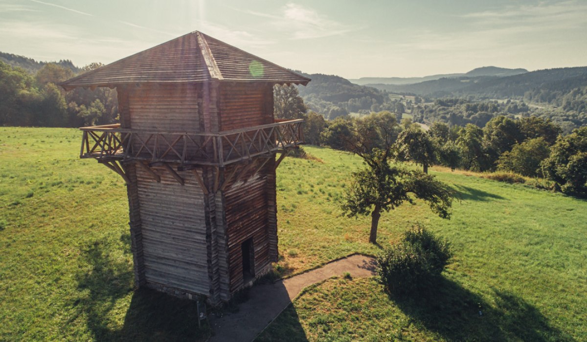 Holzwachturm auf grüner Wiese, umgeben von Bäumen und Hügeln im Hintergrund. Sonnenschein und klare Sicht., © Tourismus Ostalb