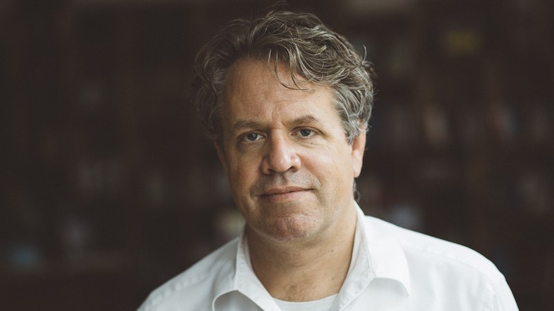 Ein Mann in einem weißen Hemd steht vor einem unscharfen Hintergrund und blickt in die Kamera., © Kulturhaus Schwanen Ein Mann in einem weißen Hemd steht vor einem unscharfen Hintergrund und blickt in die Kamera., © Kulturhaus Schwanen