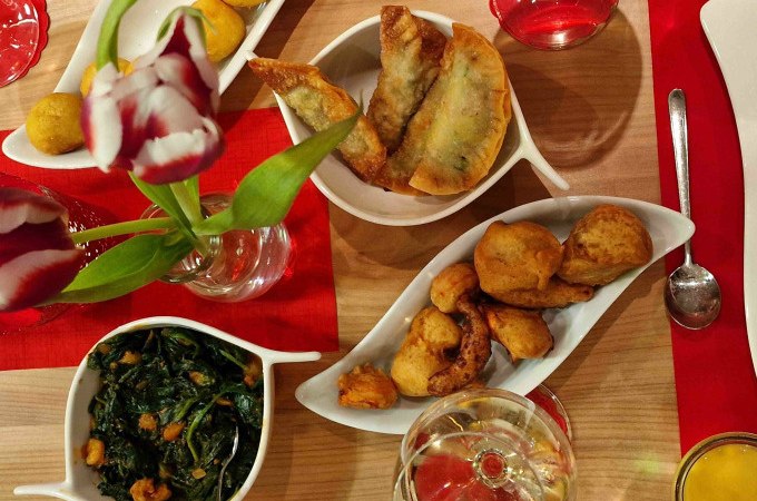 Ein Tisch mit indischen Vorspeisen wie Samosas und frittiertem Gem&uuml;se, dekoriert mit Tulpen und Getr&auml;nken. Einladende Atmosph&auml;re f&uuml;r einen Kochkurs., &copy; Kultweine-Kochwelten-Kunst&uuml;cke - Kochschule Sonja Lenz
