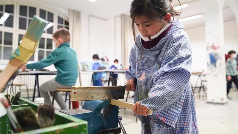 Ein Kind in einem Malkittel arbeitet konzentriert mit Holz in einem Workshop. Im Hintergrund sind weitere Kinder an Tischen zu sehen., &copy; Kunstschule Labyrinth