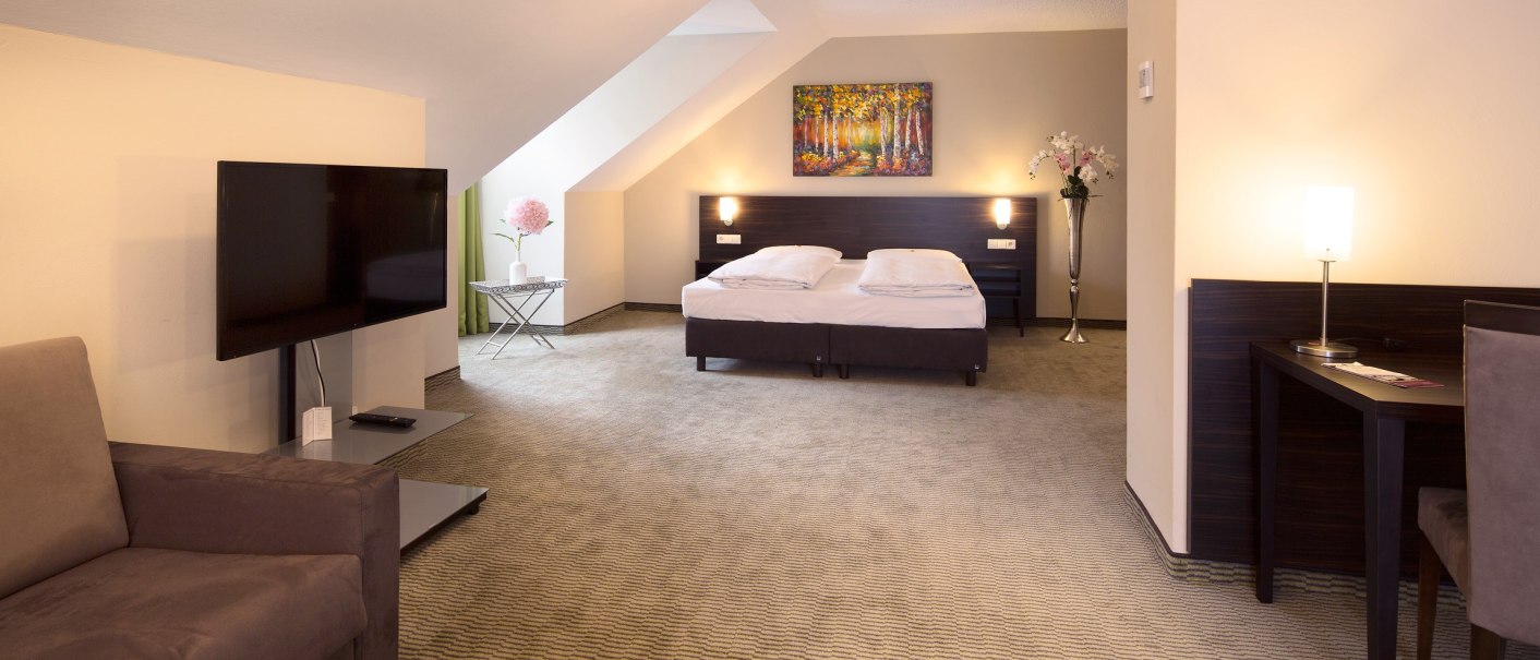 Geräumiges Hotelzimmer mit Doppelbett, Sofa, Flachbildfernseher und Schreibtisch. Helle Wände, Teppichboden und dekorative Pflanzen., © Erikson Hotel Geräumiges Hotelzimmer mit Doppelbett, Sofa, Flachbildfernseher und Schreibtisch. Helle Wände, Teppichboden und dekorative Pflanzen., © Erikson Hotel