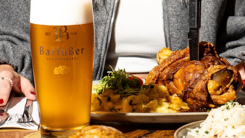 Barfüßer Bier vor einer Schweinshaxe mit Beilagen auf einem Restauranttisch., © Barfüßer Hausbrauerei Barfüßer Bier vor einer Schweinshaxe mit Beilagen auf einem Restauranttisch., © Barfüßer Hausbrauerei