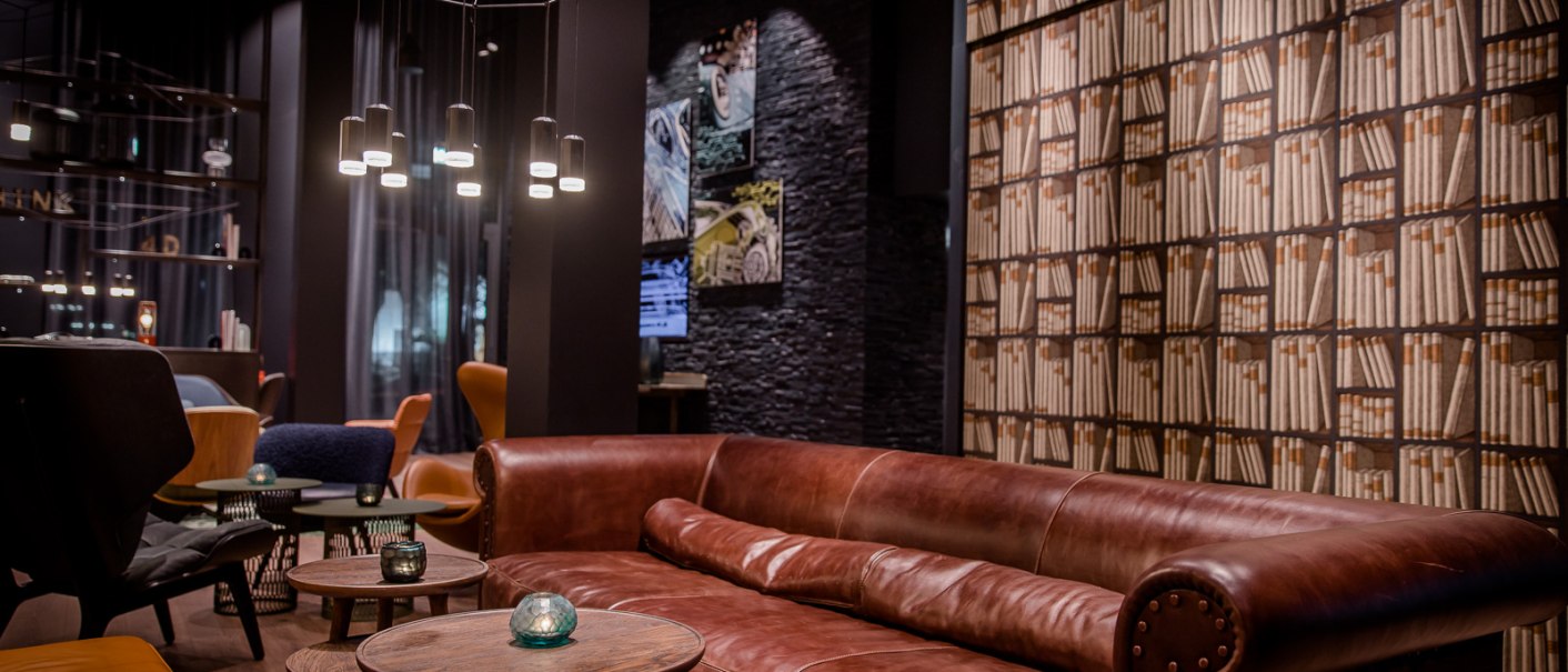 Eleganter Lounge-Bereich mit braunem Ledersofa, runden Holztischen und Bücherregal-Tapete. Moderne Beleuchtung und gemütliche Atmosphäre., © TOMAS Eleganter Lounge-Bereich mit braunem Ledersofa, runden Holztischen und Bücherregal-Tapete. Moderne Beleuchtung und gemütliche Atmosphäre., © TOMAS