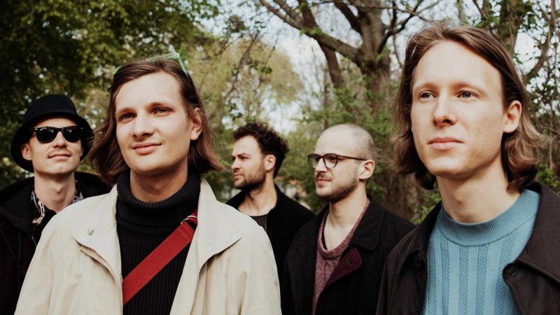 F&uuml;nf junge M&auml;nner stehen in einem Wald und blicken in verschiedene Richtungen. Sie tragen l&auml;ssige Kleidung und wirken entspannt., &copy; Foto kapelle17