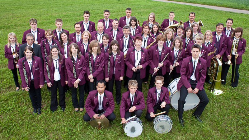 Eine gro&szlig;e Blaskapelle in lila Uniformen posiert auf einer gr&uuml;nen Wiese. Die Mitglieder halten verschiedene Blasinstrumente., &copy; Tobias Froehner