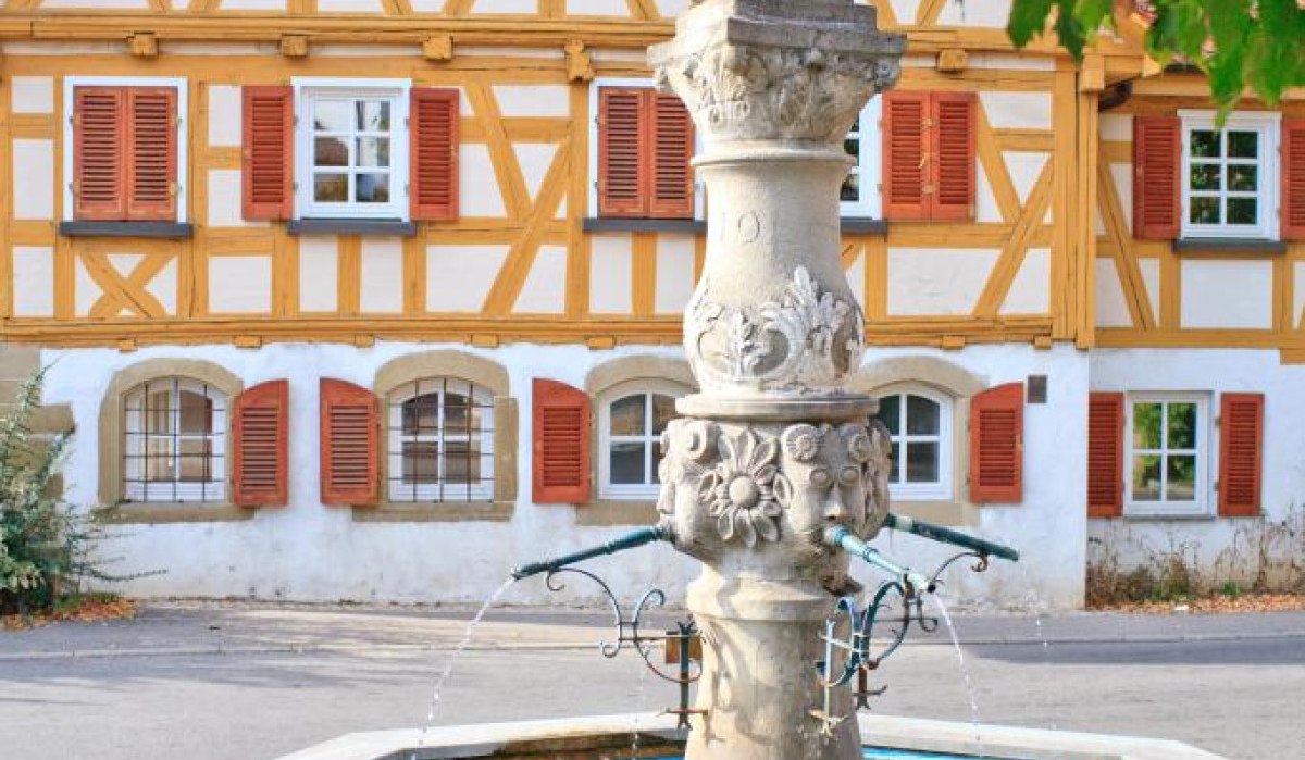 Ein steinerner Löwenbrunnen mit Wasserspeiern vor einem Fachwerkhaus, umgeben von grünen Blättern., © Waiblingen - Stuttgart-Marketing GmbH Ein steinerner Löwenbrunnen mit Wasserspeiern vor einem Fachwerkhaus, umgeben von grünen Blättern., © Waiblingen - Stuttgart-Marketing GmbH