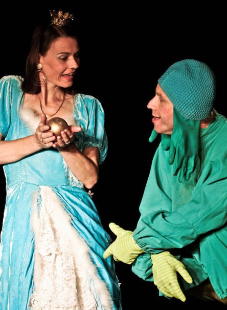 Eine Frau in einem blauen Kleid mit Krone h&auml;lt eine goldene Kugel. Neben ihr steht eine Person in einem Froschkost&uuml;m. Szene aus einem Theaterst&uuml;ck., &copy; Galli Theater Backnang