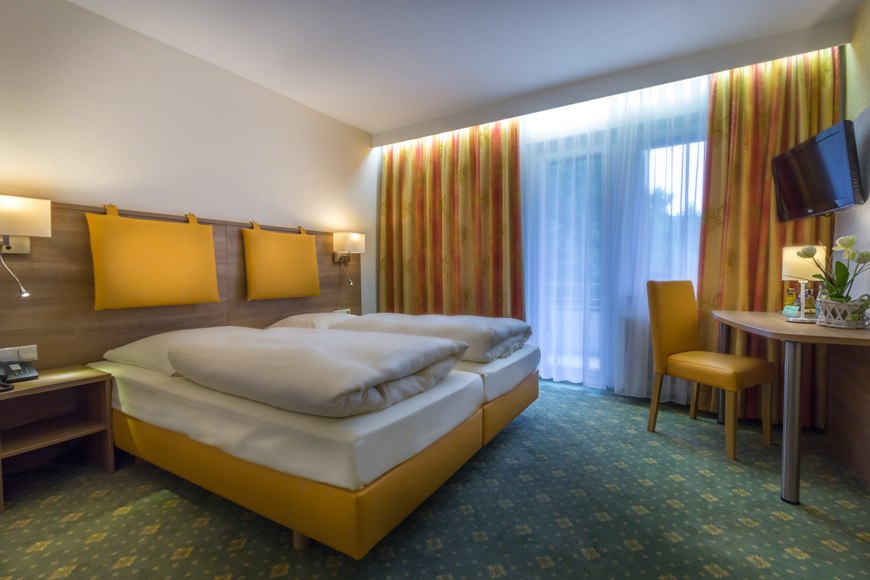 Gemütliches Doppelzimmer mit zwei Betten, Tisch, Stuhl und Fernseher. Helle Vorhänge und warme Farben schaffen eine einladende Atmosphäre., © Kulinarium an der Glems