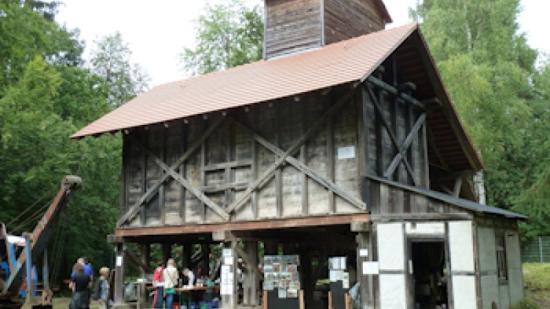 Historisches Sandwerk mit Holzkonstruktion und rotem Dach, umgeben von Bäumen. Menschen stehen davor und betrachten Ausstellungsstücke. Historisches Sandwerk mit Holzkonstruktion und rotem Dach, umgeben von Bäumen. Menschen stehen davor und betrachten Ausstellungsstücke.
