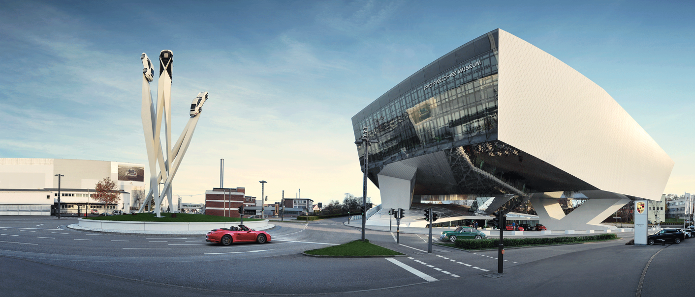 Das Porsche Museum mit seiner modernen Architektur und einer Skulptur von drei Porsche-Autos auf hohen Säulen bei Tageslicht., © Porsche AG