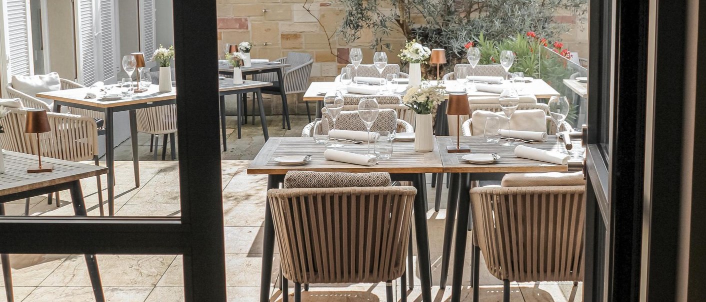 Elegante Terrasse mit gedeckten Tischen, Stühlen und Pflanzen im Hintergrund. Die Tische sind mit Gläsern, Tellern und Blumen dekoriert., © New Josch, Stuttgart