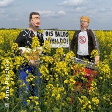 Zwei Figuren in einem bl&uuml;henden Rapsfeld, ein Schild mit der Aufschrift "Bis Baldo Ronaldo!" im Hintergrund. Humorvolle Darstellung in l&auml;ndlicher Umgebung., &copy; links im Bild