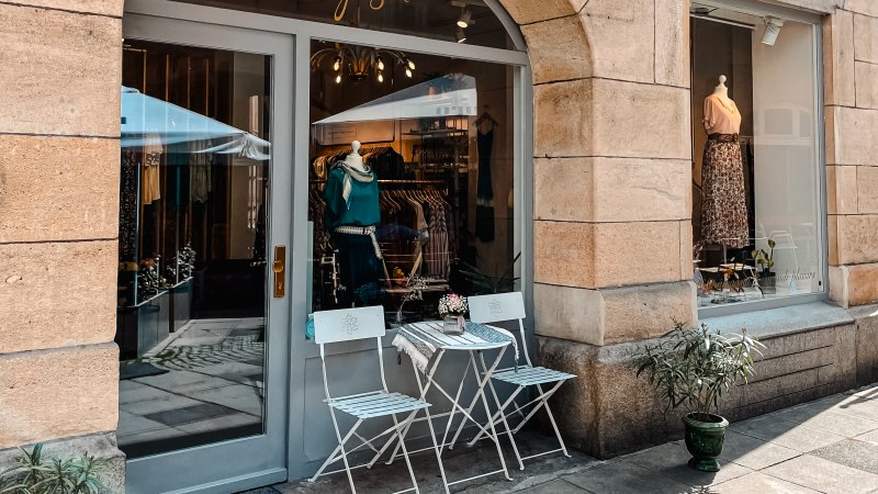 Ein kleines Ladengeschäft mit Schaufenster, dekoriert mit Kleidung. Davor stehen zwei weiße Stühle und ein Tisch auf dem Gehweg., © MAGASIN Geißstrasse 15, Stuttgart Ein kleines Ladengeschäft mit Schaufenster, dekoriert mit Kleidung. Davor stehen zwei weiße Stühle und ein Tisch auf dem Gehweg., © MAGASIN Geißstrasse 15, Stuttgart