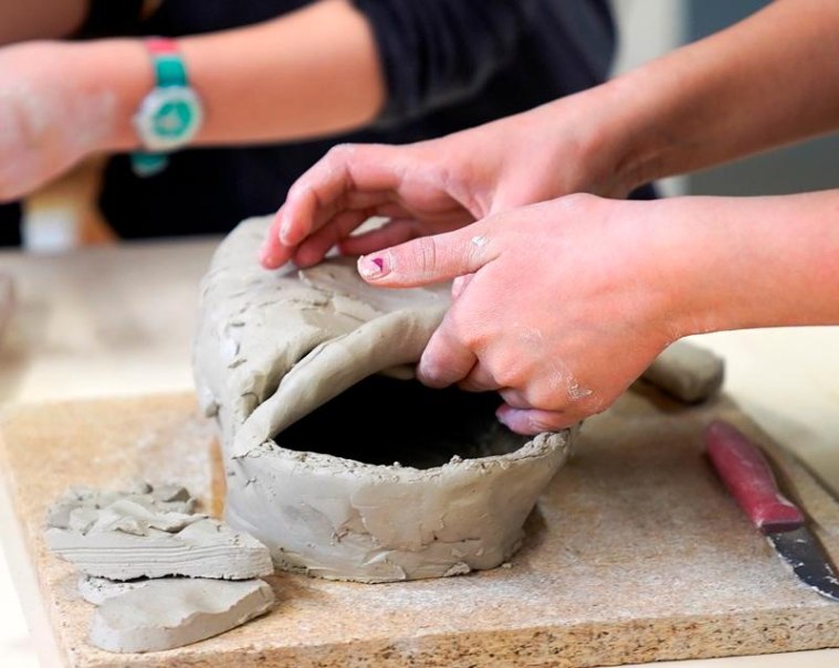 Zwei Personen formen Ton auf einem Tisch. Eine Person hält ein Stück Ton, während die andere zuschaut. Ein Messer liegt daneben., © Kunstschule Labyrinth