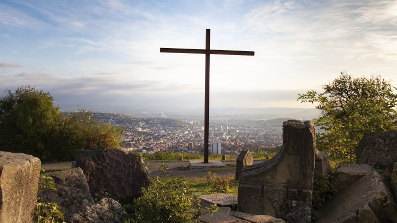 Ein Kreuz auf dem Birkenkopf in Stuttgart, umgeben von Trümmern, mit Blick auf die Stadt im Hintergrund bei Sonnenuntergang., © Stuttgart-Marketing GmbH, Jean-Claude Winkler