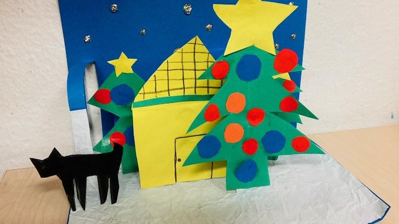 Ein buntes Pop-Up-Buch mit einem Weihnachtsbaum, einem Haus und einer schwarzen Katze aus Papier auf einem Tisch., &copy; Kunstschule Labyrinth