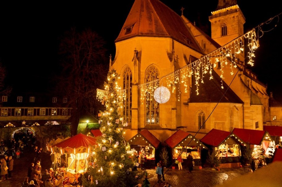 Ein festlich beleuchteter Weihnachtsmarkt mit geschm&uuml;cktem Baum, Lichterketten und einer Kirche im Hintergrund. Menschen schlendern zwischen den St&auml;nden., &copy; Stadt N&uuml;rtingen