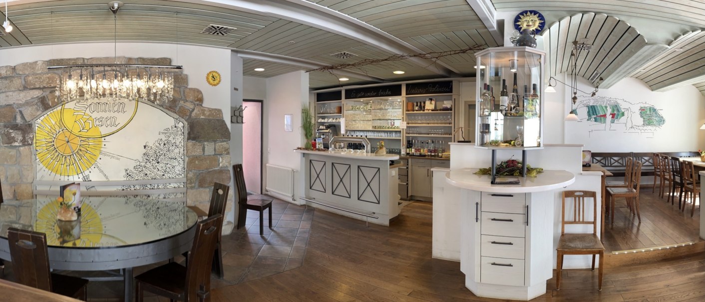 Rustikales Restaurant mit Holzmöbeln, Bar und dekorativer Wand mit "Sonnen-Besen"-Motiv. Gemütliche Atmosphäre mit Kronleuchter und Weinregal., © Weingut Zaiß