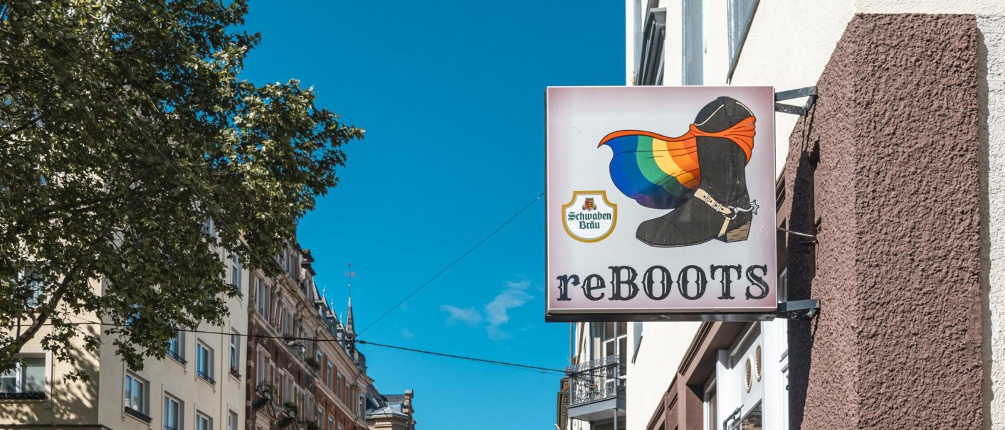 Ein Schild mit einem Stiefel und einer Regenbogenflagge, daneben die Aufschrift 'reBOOTS'. Im Hintergrund sind Geb&auml;ude und ein Baum zu sehen., &copy; SMG, Sarah Schmid