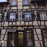 Fachwerkhaus mit der Aufschrift 'Galerie Wiedmann'. Das Gebäude hat mehrere Fenster mit grünen Fensterläden und eine Laterne an der Seite., © Galerie Wiedmann