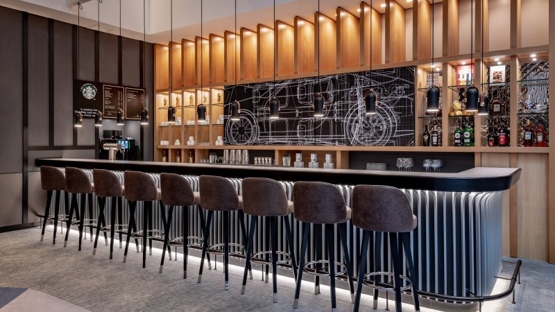 Moderne Bar mit hohen Stühlen, beleuchteten Regalen und einer Tafel mit technischen Zeichnungen im Hintergrund., © copyright by Kilian Blees