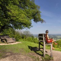 Eine Skulptur einer Frau sitzt auf einer &uuml;bergro&szlig;en Bank und blickt auf eine weite, gr&uuml;ne Landschaft unter blauem Himmel., &copy; Stuttgart-Marketing GmbH, Martina Denker