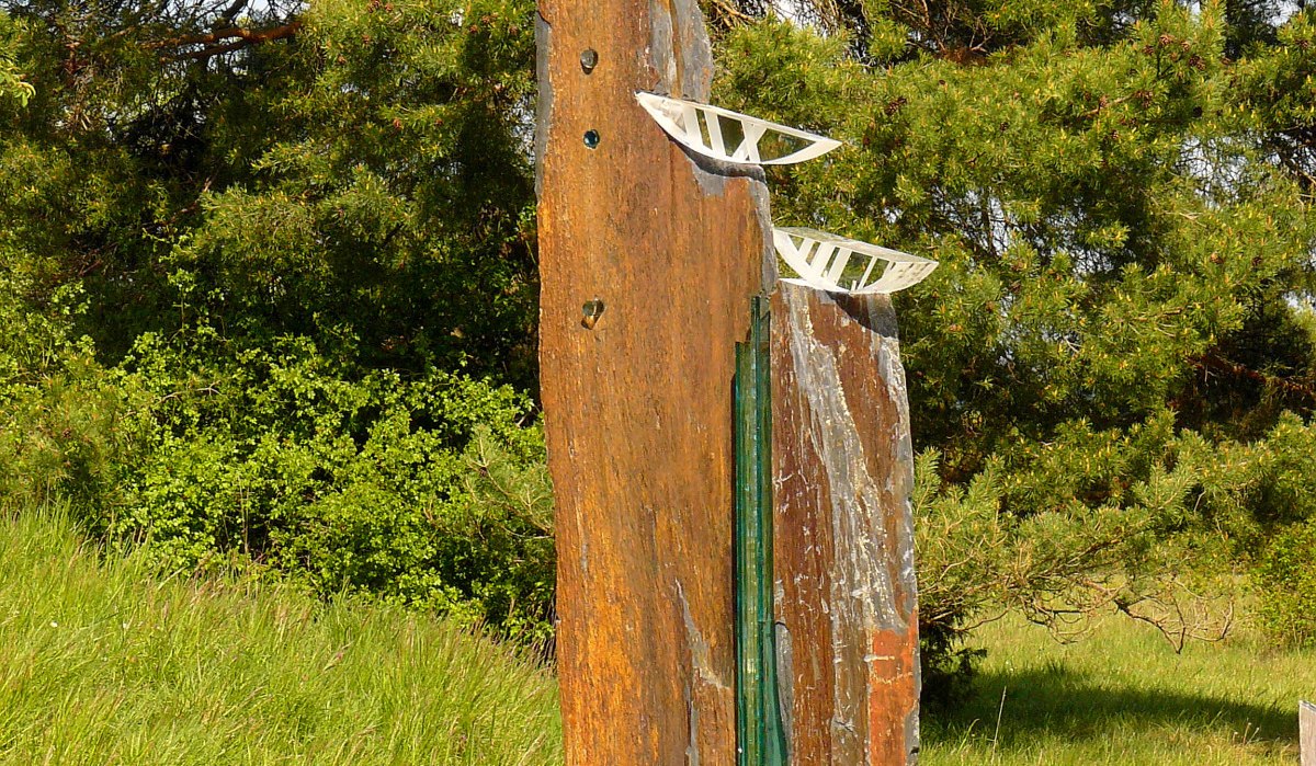 Eine Skulptur aus Stein und Glas steht auf einer grünen Wiese, umgeben von Bäumen. Die Skulptur hat weiße Elemente oben., © Natur.Nah. Schönbuch & Heckengäu