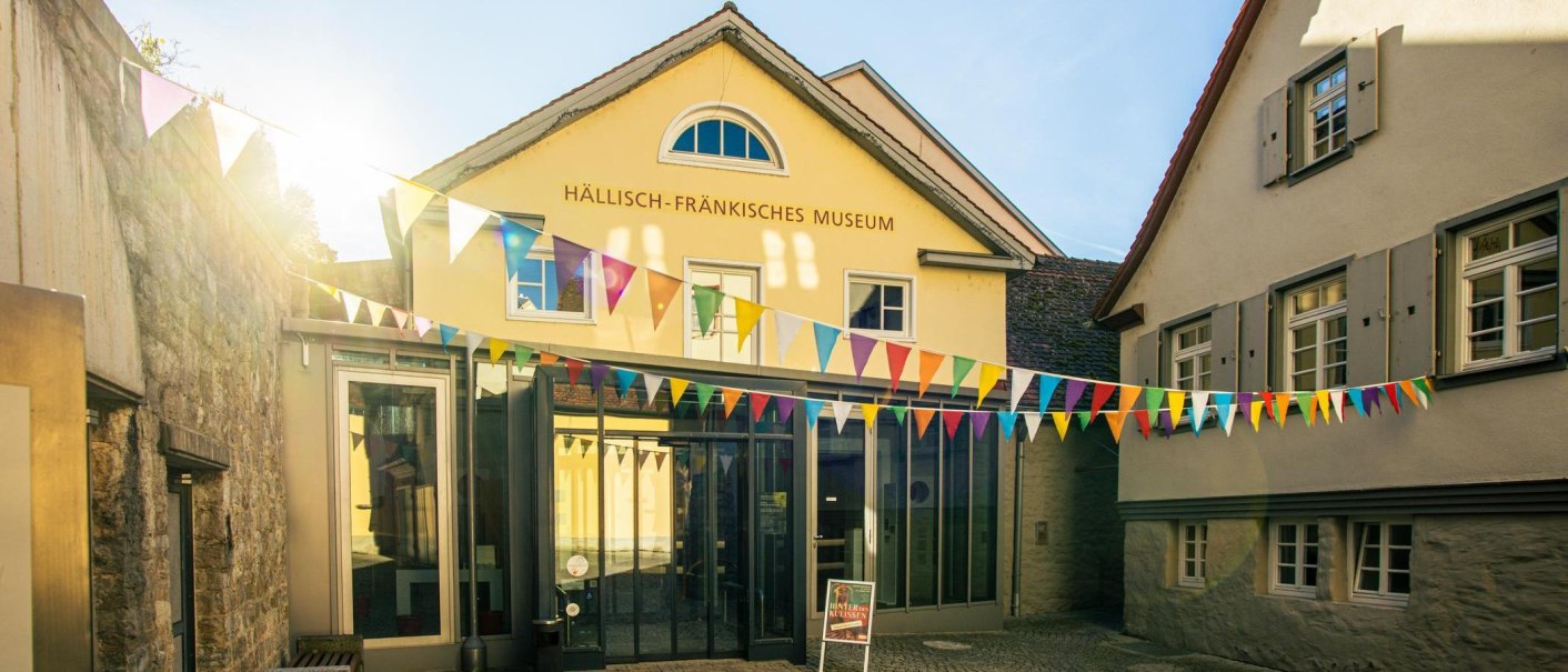 Das Hällisch-Fränkische Museum in Schwäbisch Hall, geschmückt mit bunten Wimpeln unter strahlendem Sonnenschein., © Stuttgart-Marketing GmbH, Sarah Schmid Das Hällisch-Fränkische Museum in Schwäbisch Hall, geschmückt mit bunten Wimpeln unter strahlendem Sonnenschein., © Stuttgart-Marketing GmbH, Sarah Schmid