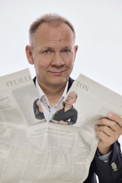 Ein Mann hält eine Zeitung, die ein Bild von ihm selbst zeigt. Er lächelt leicht und trägt ein Hemd und Sakko., © Stadtverwaltung Vaihingen an der Enz Ein Mann hält eine Zeitung, die ein Bild von ihm selbst zeigt. Er lächelt leicht und trägt ein Hemd und Sakko., © Stadtverwaltung Vaihingen an der Enz