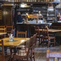 Gem&uuml;tlicher Innenraum eines Restaurants mit Holztischen und -st&uuml;hlen, einer Bar im Hintergrund und einem gro&szlig;en Kachelofen links., &copy; SMG, Sarah Schmid