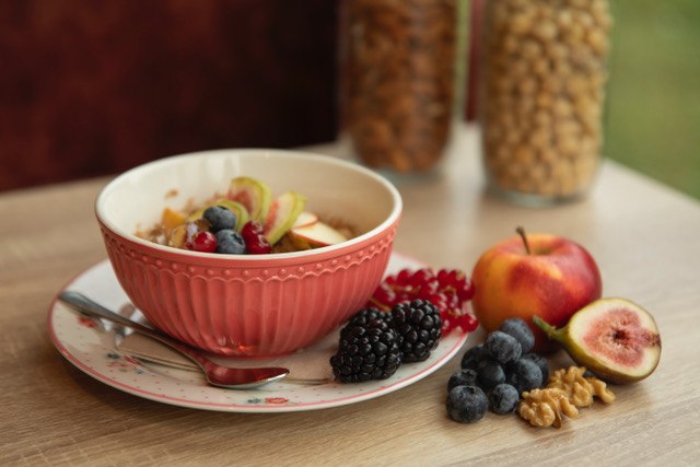 Eine Schale mit Müsli, Beeren und Nüssen auf einem Tisch. Daneben liegen ein Apfel, Feige, Brombeeren und Walnüsse., © Ingrid Glückswelt