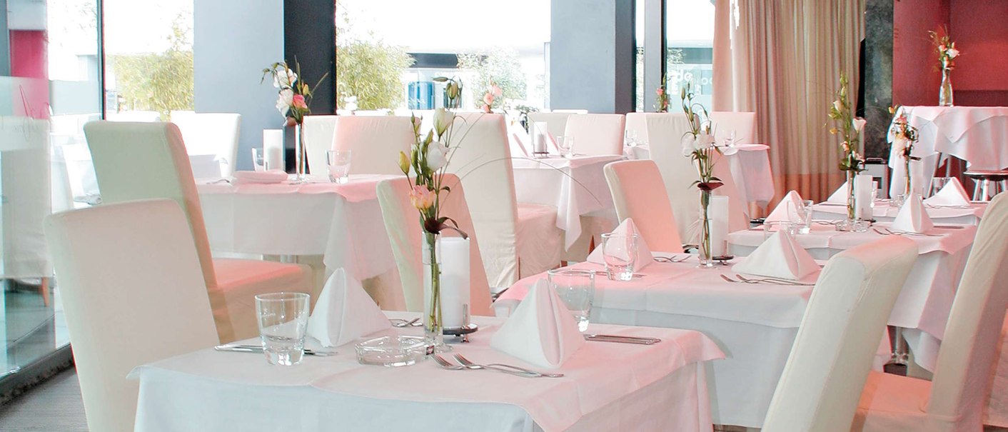 Elegantes Restaurant mit weißen Tischdecken, stilvoll gedeckten Tischen und Blumenarrangements. Helle, moderne Einrichtung mit großen Fenstern., © AMICI Elegantes Restaurant mit weißen Tischdecken, stilvoll gedeckten Tischen und Blumenarrangements. Helle, moderne Einrichtung mit großen Fenstern., © AMICI