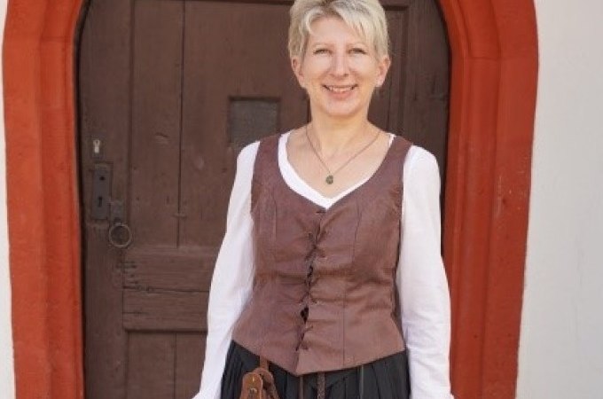 Eine Frau in historischer Kleidung steht l&auml;chelnd vor einer alten Holzt&uuml;r mit rotem Rahmen., &copy; Stadtverwaltung Weil der Stadt