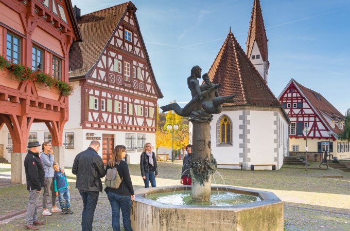 Eine Gruppe von Menschen betrachtet einen Brunnen auf einem historischen Platz in Plochingen. Fachwerkh&auml;user und eine Kirche im Hintergrund., &copy; PlochingenInfo