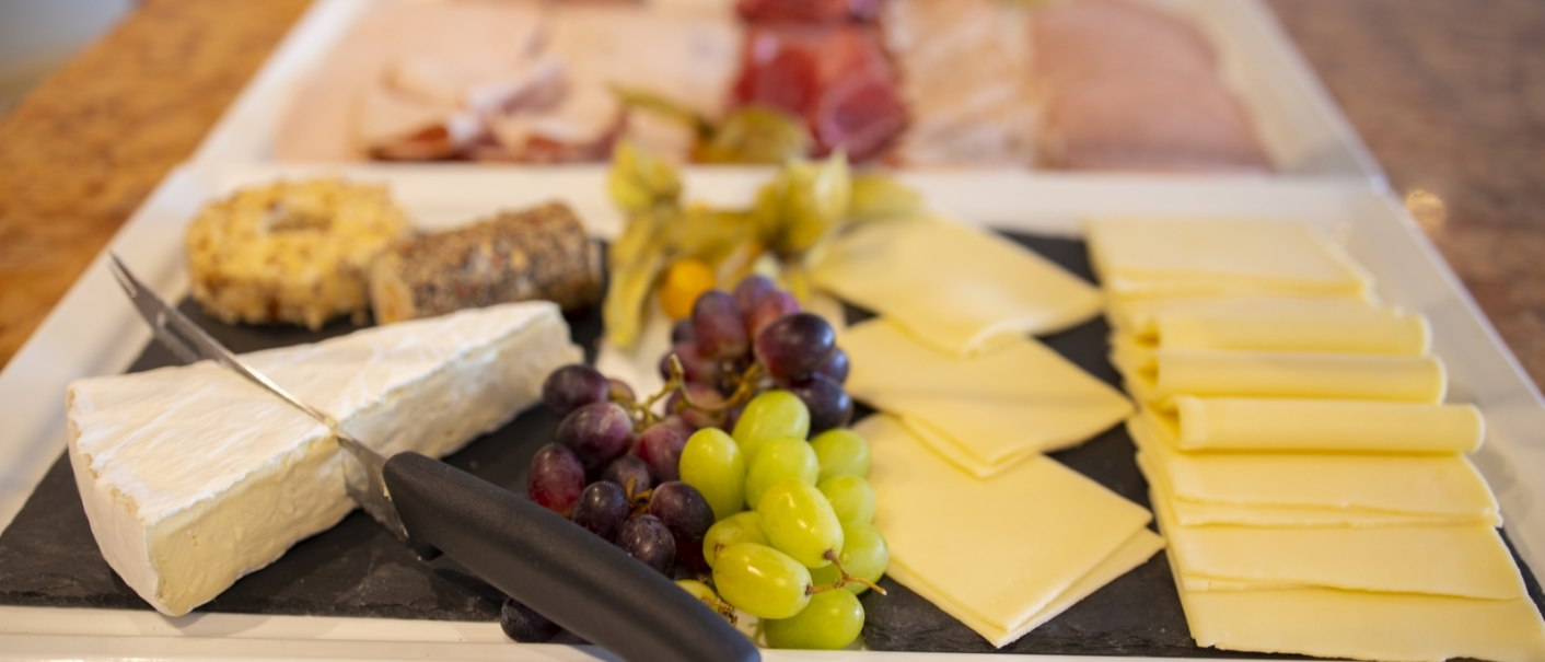 Ein Frühstücksbuffet mit verschiedenen Käsesorten, Trauben und Aufschnitt. Im Vordergrund liegt ein Messer auf einem Stück Brie., © Hotel Gloria GmbH Restaurant Möhringer Hexle