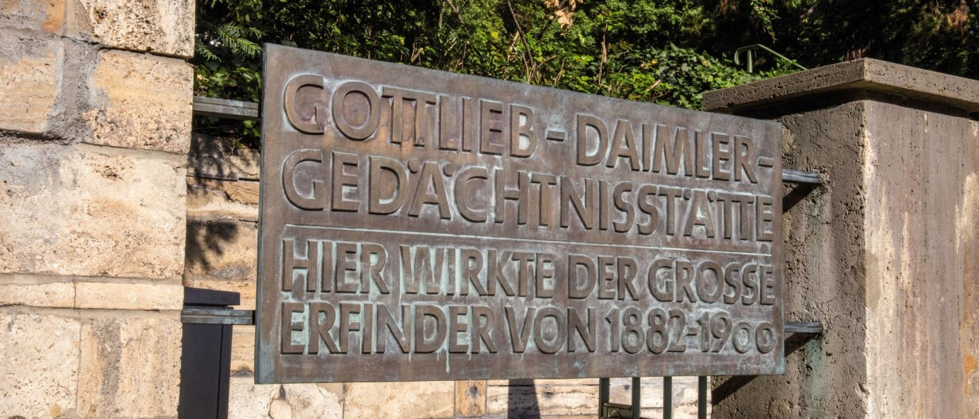 Metallschild an einer Steinmauer mit der Aufschrift 'Gottlieb-Daimler-Gedächtnisstätte'. Umgeben von grüner Vegetation., © Stuttgart-Marketing GmbH Achim Mende Metallschild an einer Steinmauer mit der Aufschrift 'Gottlieb-Daimler-Gedächtnisstätte'. Umgeben von grüner Vegetation., © Stuttgart-Marketing GmbH Achim Mende