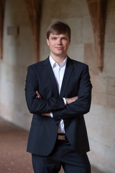 Ein Mann in einem schwarzen Anzug steht mit verschränkten Armen in einem überdachten Gang mit Steinwänden., © Stadtverwaltung Vaihingen an der Enz Ein Mann in einem schwarzen Anzug steht mit verschränkten Armen in einem überdachten Gang mit Steinwänden., © Stadtverwaltung Vaihingen an der Enz