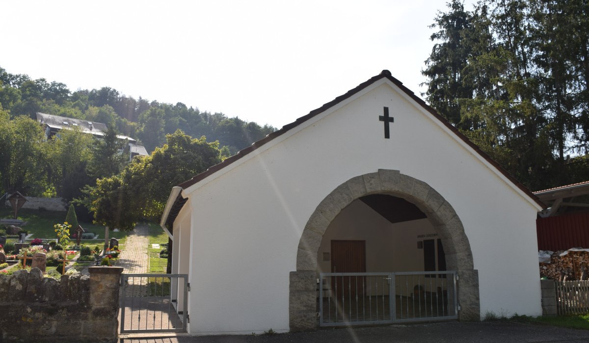 Weiße Kapelle mit Kreuz, umgeben von Bäumen und einem Friedhof. Ein Weg führt durch das Gelände. Im Hintergrund sind Hügel und Gebäude zu sehen., © Land der 1000 Hügel - Kraichgau-Stromberg Weiße Kapelle mit Kreuz, umgeben von Bäumen und einem Friedhof. Ein Weg führt durch das Gelände. Im Hintergrund sind Hügel und Gebäude zu sehen., © Land der 1000 Hügel - Kraichgau-Stromberg