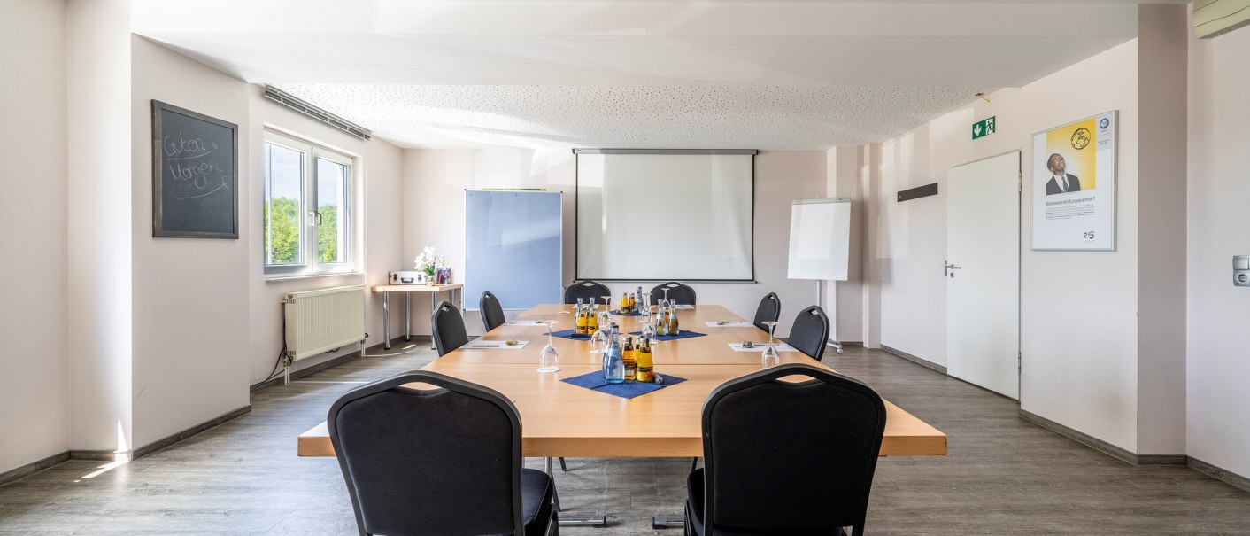 Tagungsraum mit großem Tisch, Stühlen, Getränken und Präsentationstechnik. Fenster lassen Tageslicht herein, an der Wand hängt eine Tafel mit 'Guten Morgen'., © Plaza INN Stuttgart-Filderstadt Tagungsraum mit großem Tisch, Stühlen, Getränken und Präsentationstechnik. Fenster lassen Tageslicht herein, an der Wand hängt eine Tafel mit 'Guten Morgen'., © Plaza INN Stuttgart-Filderstadt
