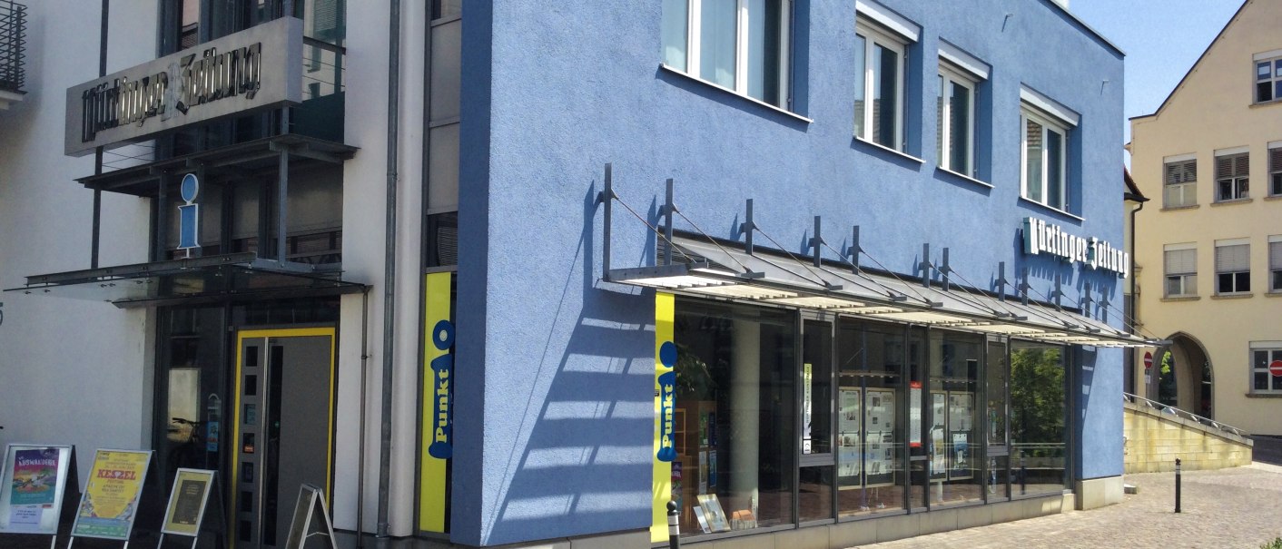 Blaues Gebäude mit Glasfassade und Schildern 'i-Punkt' und 'Zeitung'. Pflastersteinstraße und weitere Gebäude im Hintergrund., © J. Tubolzer Blaues Gebäude mit Glasfassade und Schildern 'i-Punkt' und 'Zeitung'. Pflastersteinstraße und weitere Gebäude im Hintergrund., © J. Tubolzer