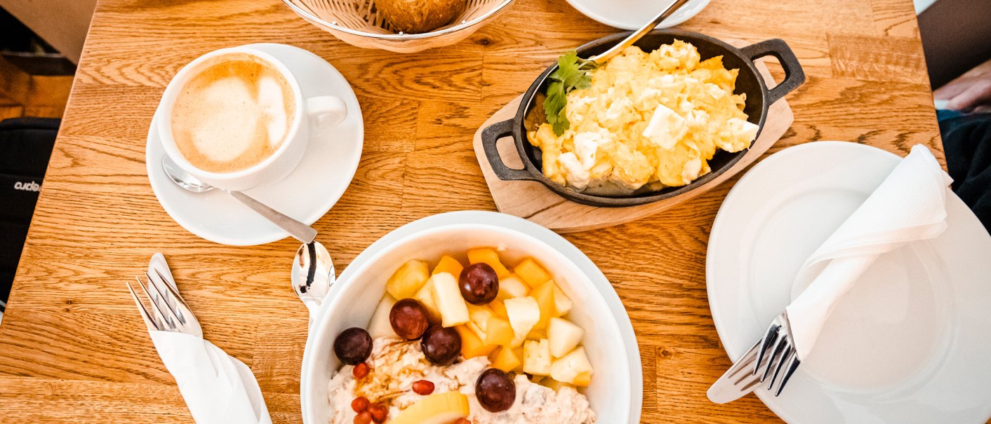 Ein Frühstückstisch mit einer Tasse Kaffee, Rührei in einer Pfanne und einem Obstsalat in einer Schüssel auf einem Holztisch., © Stuttgart-Marketing GmbH, Sarah Schmid Ein Frühstückstisch mit einer Tasse Kaffee, Rührei in einer Pfanne und einem Obstsalat in einer Schüssel auf einem Holztisch., © Stuttgart-Marketing GmbH, Sarah Schmid